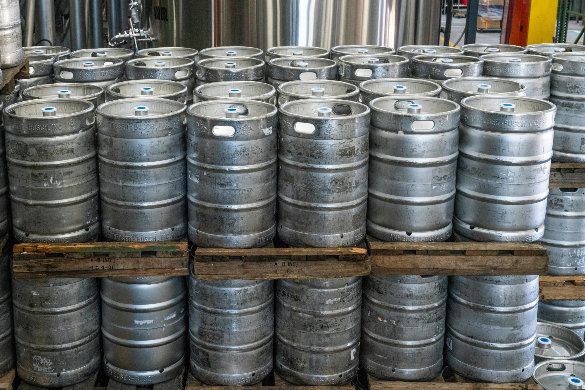 Steel kegs neatly stacked on pallets in an industrial brewery warehouse.