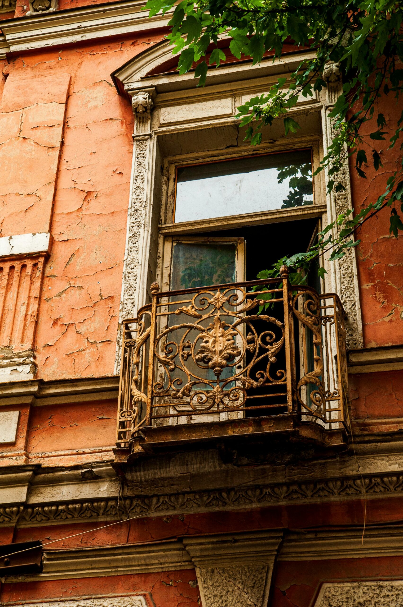 An ornate iron balcony attached to an aged, orange-colored building facade.