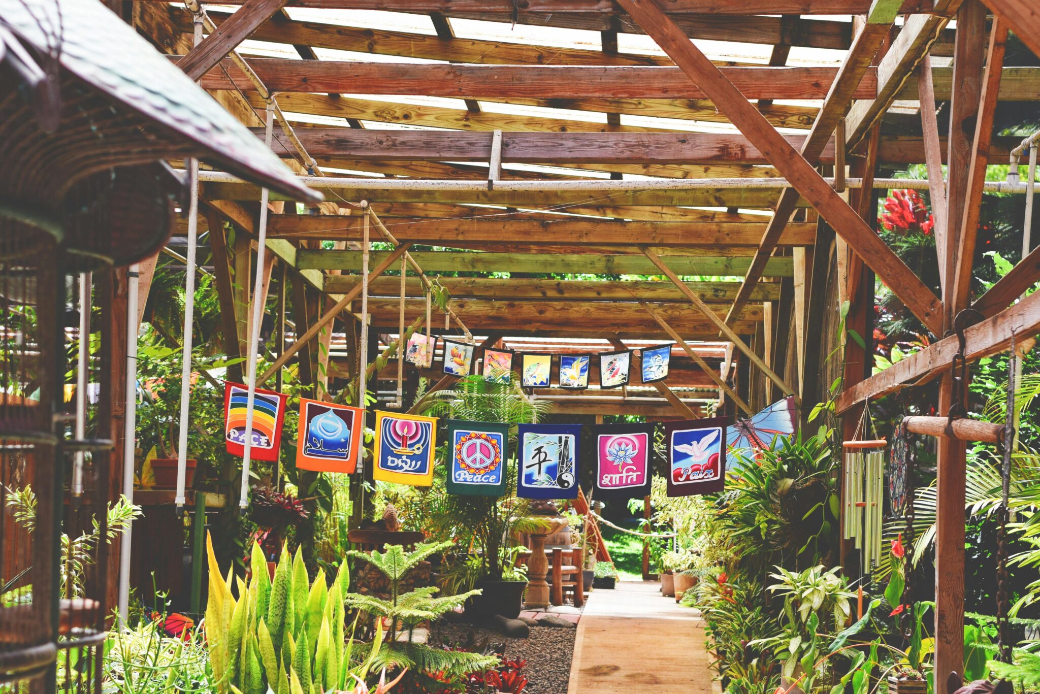 A vibrant outdoor market scene with flags and lush plants under a wooden structure.