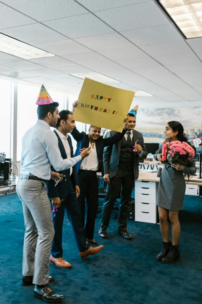 A joyous office birthday celebration with colleagues surprising a coworker with a sign and flowers.